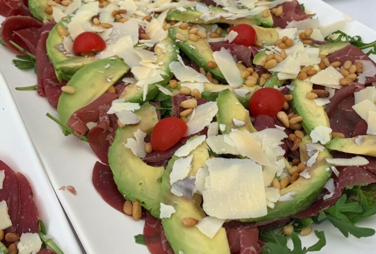 Bresaola-Schinken mit Avocado, gerösteten Pinienkernen und gehobeltem Parmesan, Rucola-Garnitur und Olivenöl